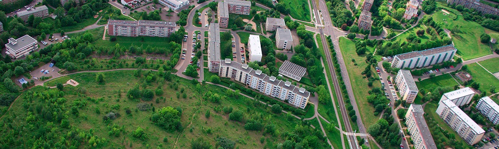 Mehrere Mehrfamilienhäuser in Blocks, dazwischen Grünflächen und eine Bahnlinie, von oben Fotografiert.